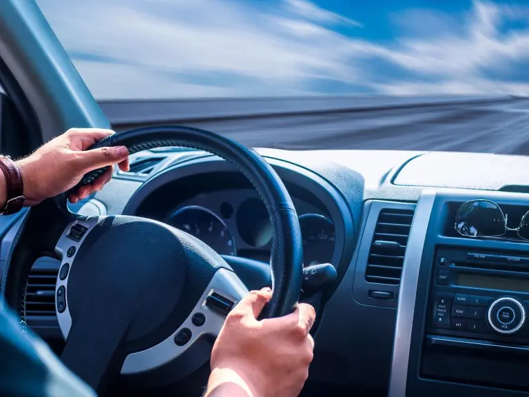 A person is driving in the car while holding on to their steering wheel.